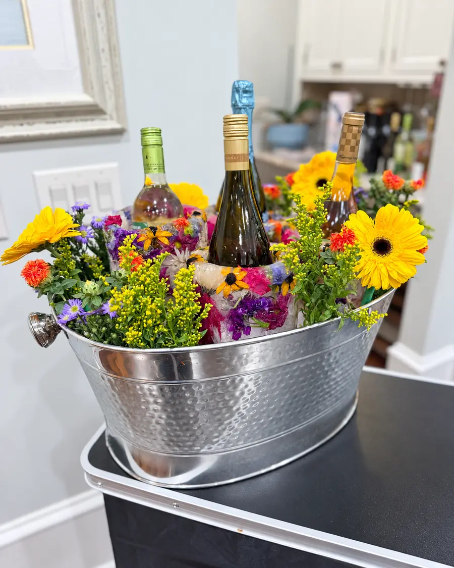Champagne and wine bottles displayed in handcrafted flower-filled ice chillers with fresh complementary florals